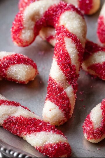 Candy Cane Cookie Recipe | Soft, Festive & Easy to Make 3 Candy Cane Cookie A close-up of freshly baked candy cane-shaped cookies on a tray, glistening with sparkling sugar.