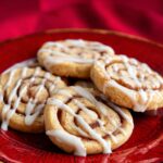 Cinnamon Roll Cookies Plate of cinnamon roll cookies topped with white icing drizzle on a red textured plate