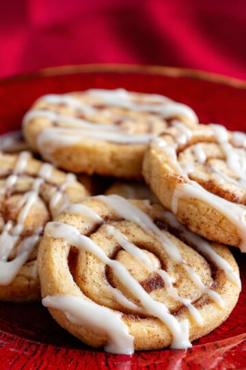 Delicious Cinnamon Roll Cookies Recipe 23 Cinnamon Roll Cookies Plate of cinnamon roll cookies topped with white icing drizzle on a red textured plate