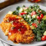 Hot Honey Chicken Crispy breaded chicken cutlet drizzled with hot honey, served on a plate alongside a chopped kale salad with cherry tomatoes and avocado.