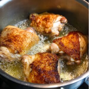 Easy Chicken Paprikash Recipe | Traditional Hungarian 15 Chicken thighs browning in a stainless steel pot, crispy golden skin sizzling in butter and oil during the cooking process