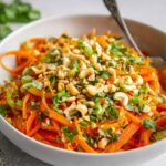 Korean Carrot Salad with julienned carrots, bell peppers, cilantro, green onions, and chopped cashews in a white bowl