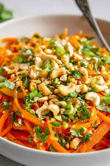 Easy Korean Carrot Salad Recipe 20 Korean Carrot Salad with julienned carrots, bell peppers, cilantro, green onions, and chopped cashews in a white bowl