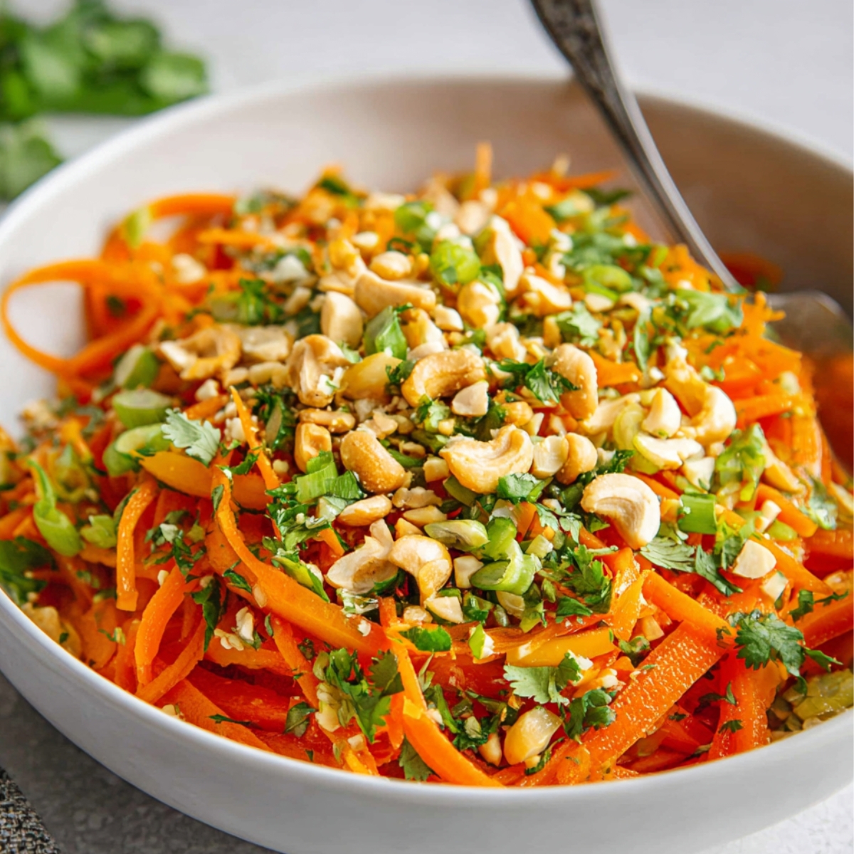 Korean Carrot Salad with julienned carrots, bell peppers, cilantro, green onions, and chopped cashews in a white bowl