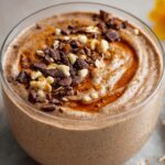 Blended Oats Recipe Creamy blended oats in a glass, topped with chopped chocolate, nuts, and a swirl of syrup for a dessert-like breakfast.