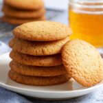 Honey Cookies A stack of freshly baked golden honey cookies on a plate, with a honey jar and dipper in the background.
