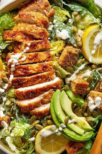 Honey Hot Chicken Salad Recipe | Crispy & Spicy in 30 Min 1 Honey Hot Chicken Salad Finished hot honey chicken Caesar salad with sliced crispy chicken, romaine lettuce, croutons, avocado slices, pumpkin seeds, lemon wedges, and creamy dressing in a large bowl.