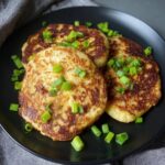 Irish Potato Pancakes Three crispy golden boxty pancakes topped with green onions on a black plate. The pancakes are perfectly browned and fluffy inside.