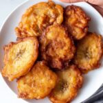 Jamaican banana fritters A close-up of a plate filled with golden, crispy Jamaican banana fritters. The fritters are crispy on the outside with a soft, warm interior.