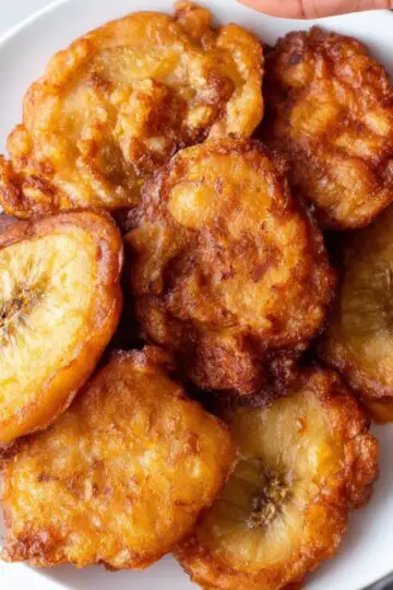 Jamaican banana fritters A close-up of a plate filled with golden, crispy Jamaican banana fritters. The fritters are crispy on the outside with a soft, warm interior.