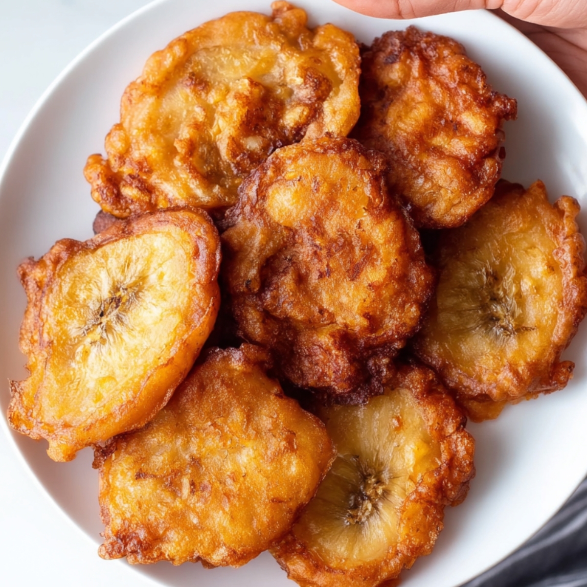 Jamaican banana fritters A close-up of a plate filled with golden, crispy Jamaican banana fritters. The fritters are crispy on the outside with a soft, warm interior.