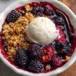 Mixed Berry Crisp With Frozen Berries Warm mixed berry crisp in a small dish topped with vanilla ice cream, showing bubbling berries, golden oat crumble, and a spoon on the side.