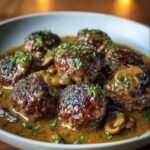 Salisbury Steak Meatballs Golden-browned meatballs coated in rich mushroom gravy, garnished with chopped parsley and served in a shallow bowl.