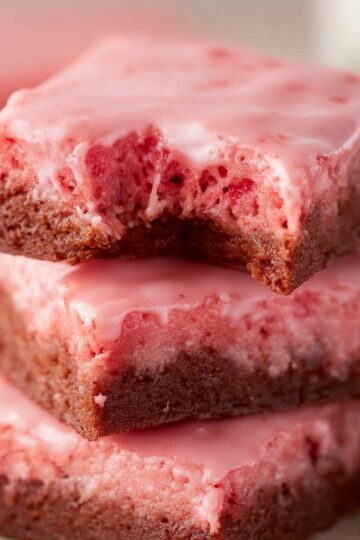 Strawberry Brownies Recipe | Soft, Pink & Ready in 30 Min 6 Strawberry Brownies Stacked strawberry brownies with pink glaze, one brownie bitten to show the moist and chewy texture inside.