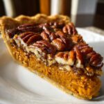 Sweet Potato Pecan Pie Slice of sweet potato pecan pie on a plate highlighting the two distinct layers and glossy pecan topping, with the full pie in the background.