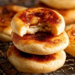 creme brûlée cookies stacked on a wire rack, topped with caramelized sugar, with one cookie bitten to show a soft buttery interior.