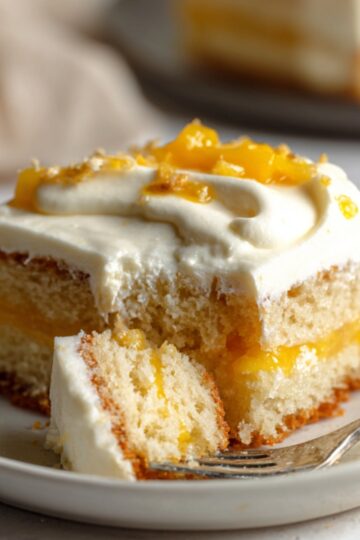 Easy Mango Tres Leches Recipe | Tropical Summer Dessert 22 mango tres leches cake slice on a plate with a fork and a bite removed, showing moist sponge and creamy layers.