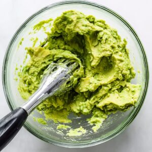 Healthy Avocado Chicken Wrap Recipe | 10-Minute Lunch 15 Fresh mashed avocado in a glass bowl with an avocado masher, photographed from above on a light background.