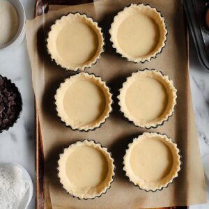 Boston Cream Pie Cookies Recipe | Easy & Delicious 18 “Top-down food photography of unbaked cookie tart shells filled with smooth vanilla custard on a parchment-lined baking tray, baking ingredients around, clean marble countertop, soft natural light”