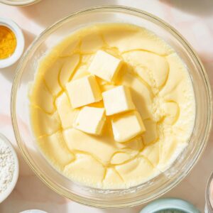 Boston Cream Pie Cookies Recipe | Easy & Delicious 19 “Overhead view of creamy vanilla custard mixture in a glass bowl with butter pieces melting on top, surrounded by small bowls of baking ingredients, bright kitchen lighting, editorial food style”