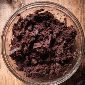 Dark chocolate cookie dough with visible chocolate chunks in a glass bowl on a wooden table.