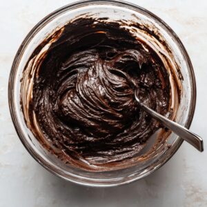 Healthy Chocolate Marshmallow Swirl Cookies Recipe 15 "A glass mixing bowl with thick, dark chocolate cookie batter, showing smooth consistency with a spoon inserted into the mixture."