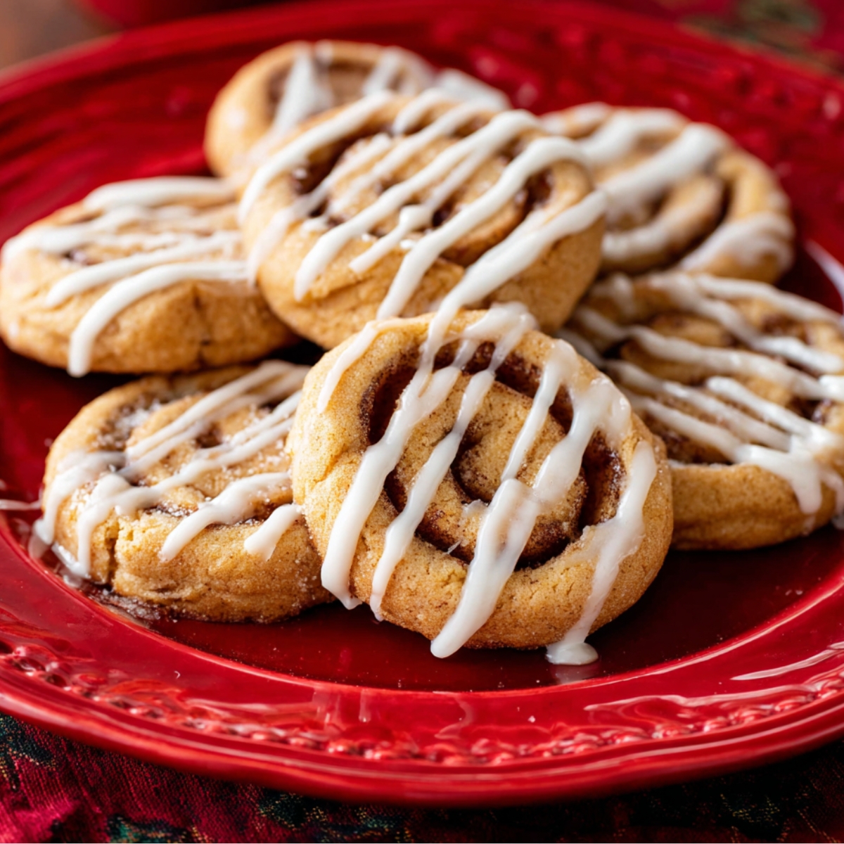 Delicious Cinnamon Roll Cookies Recipe 13 Cinnamon roll cookies drizzled with white icing arranged on a red decorative plate.