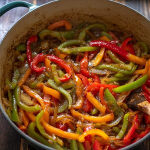 Delicious Cuban Ropa Vieja Recipe 17 Colorful bell peppers and onions sautéing in a Dutch oven, showcasing red, yellow, and green peppers cooking in a savory sauce.