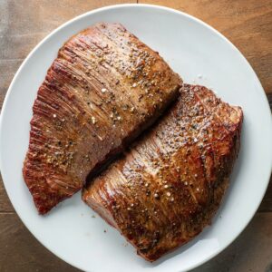 Delicious Cuban Ropa Vieja Recipe 16 Two perfectly seared pieces of flank steak on a white plate, seasoned with salt and pepper, ready to be added to the Cuban Ropa Vieja dish.