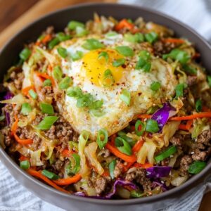 The Best Egg Roll In A Bowl Recipe 17 A bowl of egg roll in a bowl featuring ground meat, shredded cabbage, carrots, and purple cabbage, topped with a crispy fried egg and green onions.