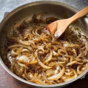Best French Onion Pasta Recipe In 30 Minutes 15 Caramelized sliced onions cooking in a skillet with a wooden spoon, showing deep golden-brown color.