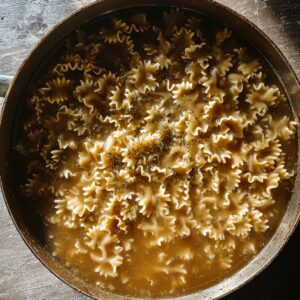 Best French Onion Pasta Recipe In 30 Minutes 16 Farfalle pasta simmering in savory broth inside a wide metal pan, photographed from above.