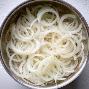 Best French Onion Pasta Recipe In 30 Minutes 14 Thinly sliced raw white onions arranged in a saucepan before cooking, photographed from a top-down view.
