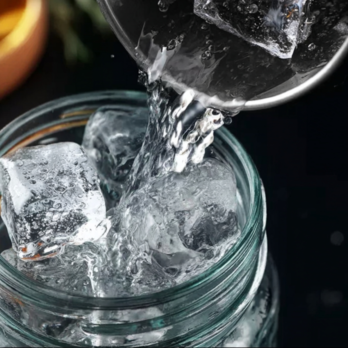 Easy Gingerbread White Russian Recipe - Holiday Cocktail 10 Close-up action shot of clear liquid being poured over large ice cubes into a glass jar, cocktail preparation scene, crisp ice texture, realistic water splash, dark elegant background, shallow depth of field, professional drink photography, ultra realistic, high detail, studio lighting