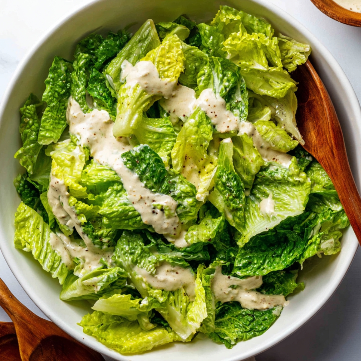Honey Hot Chicken Salad Recipe | Crispy & Spicy in 30 Min 13 Chopped romaine lettuce tossed with creamy Caesar dressing in a white bowl, wooden salad spoons on the side.
