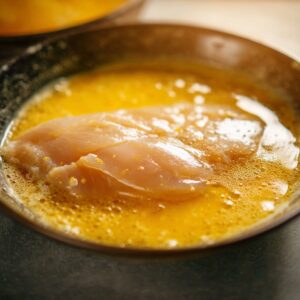 Healthy Hot Honey Chicken Recipe In 30 Minutes 17 Uncooked chicken cutlet coated in flour inside a shallow bowl, with loose flour spread around the edges.