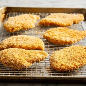 Healthy Hot Honey Chicken Recipe In 30 Minutes 19 Breaded chicken cutlets arranged on a wire rack over a baking sheet, showing even coating and ready for baking.