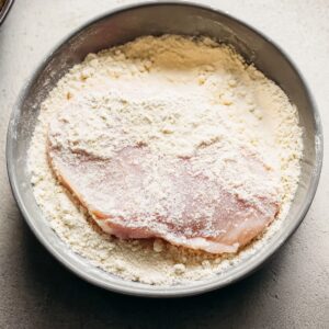 Healthy Hot Honey Chicken Recipe In 30 Minutes 16 Raw chicken breast resting in a bowl of beaten eggs, with bubbles and glossy texture visible on the surface.