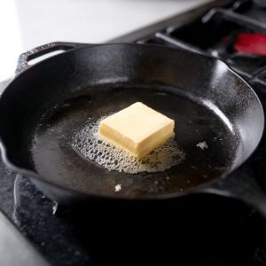 The Best Irish Potato Pancakes Recipe 17 "A square of butter melting in a cast iron skillet, preparing for cooking boxty pancakes. The sizzling butter adds rich flavor to the dish."