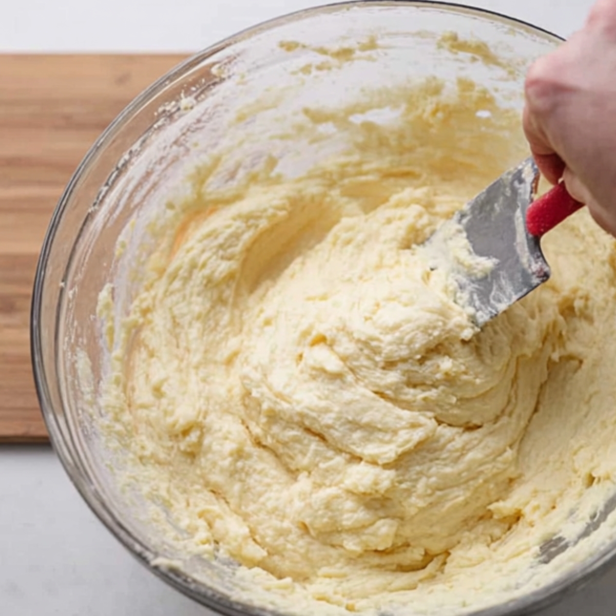 The Best Irish Potato Pancakes Recipe 10 "A person mixing boxty pancake batter in a clear mixing bowl using a spatula. The thick, creamy batter is ready to be cooked."