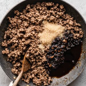 Easy Korean Ground Beef Bowl Recipe | 20-Minute Dinner 15 Top-down view of browned ground beef cooking in a skillet, with sugar and dark sauce added on one side.