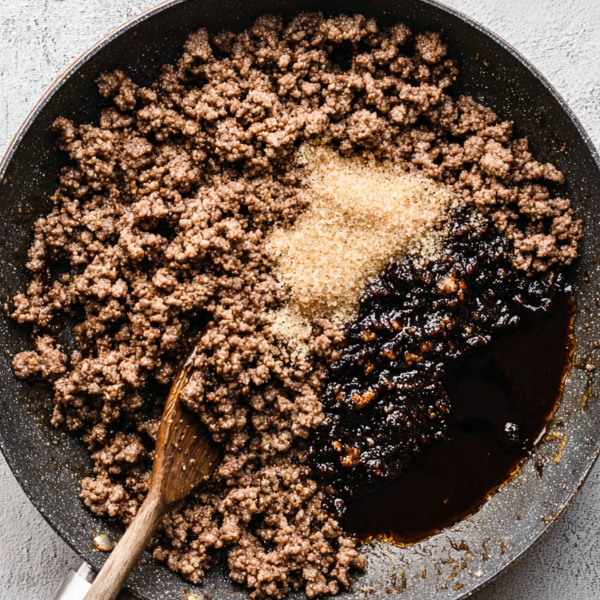 Easy Korean Ground Beef Bowl Recipe | 20-Minute Dinner 11 Top-down view of browned ground beef cooking in a skillet, with sugar and dark sauce added on one side.