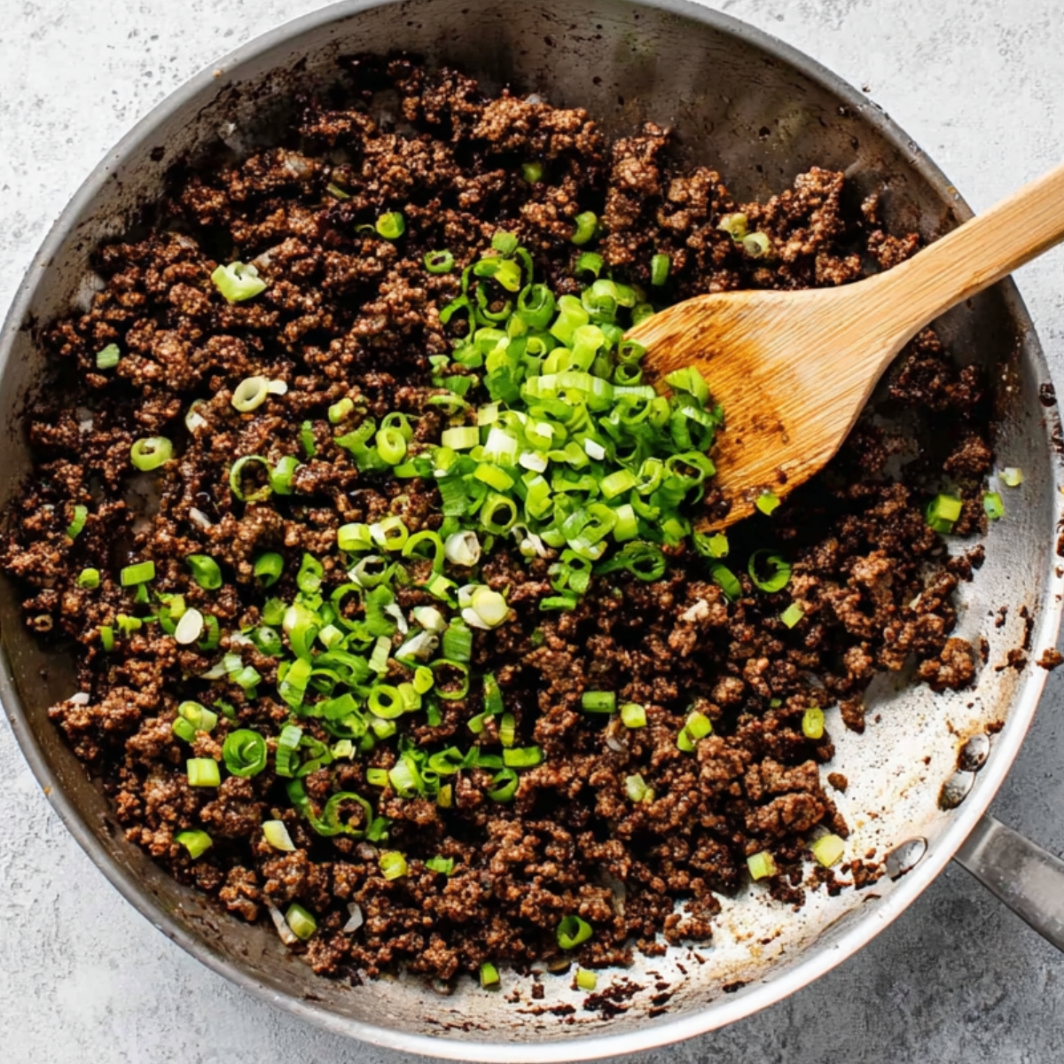 Easy Korean Ground Beef Bowl Recipe | 20-Minute Dinner 12 Cooked ground beef in a pan topped with freshly chopped green onions, being stirred with a wooden spoon.