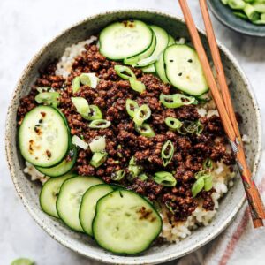 Easy Korean Ground Beef Bowl Recipe | 20-Minute Dinner 17 Korean ground beef served over white rice, topped with sliced cucumbers and green onions, with chopsticks on the bowl.
