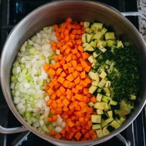 Easy Minestrone Soup Recipe | Better Than Restaurant 15 Pot filled with chopped onions, carrots, zucchini, celery, and fresh herbs ready to cook for minestrone soup.
