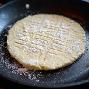 The Best Scottish Tattie Scones Recipe (Just 3 Ingredients!) 18 Scottish tattie scone dough flattened into a round shape in a frying pan. The dough is lightly dusted with flour and ready to be cooked to a golden perfection