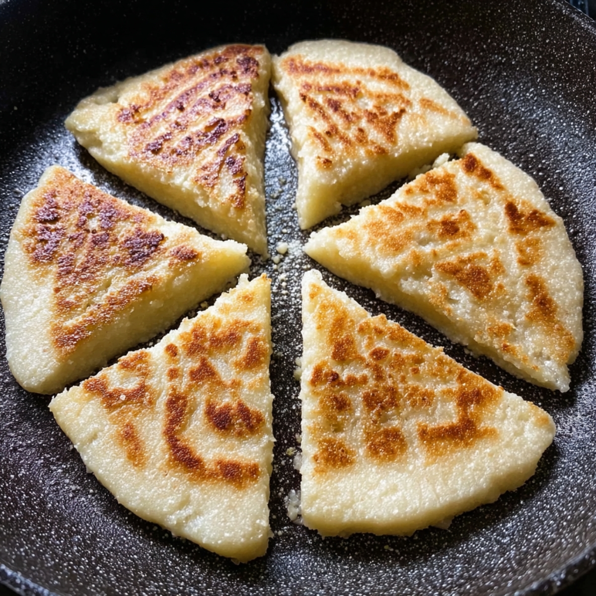 The Best Scottish Tattie Scones Recipe (Just 3 Ingredients!) 13 Scottish tattie scones frying in a pan, forming crispy, golden-brown crusts with slightly charred marks. The scones are cut into triangular sections.