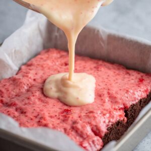 Strawberry Brownies Recipe | Soft, Pink & Ready in 30 Min 19 Strawberry glaze being poured over baked strawberry brownies in a pan, creating a smooth glossy topping.