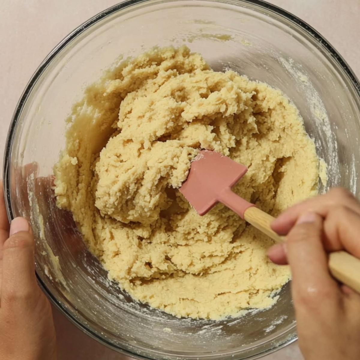 Creme Brûlée Cookies Recipe | Easy & Addictive 11 Hands mixing soft cookie dough in a glass bowl using a spatula, shown in a top-down kitchen view.