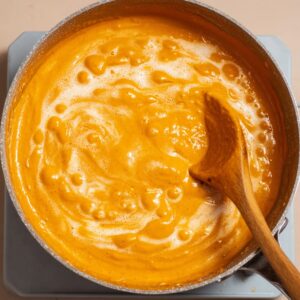 Best Gochujang Pasta Recipe | Creamy & Spicy in 20 Minutes 18 Creamy orange sauce simmering in a saucepan, swirled with a wooden spoon, smooth and velvety texture, overhead view.
